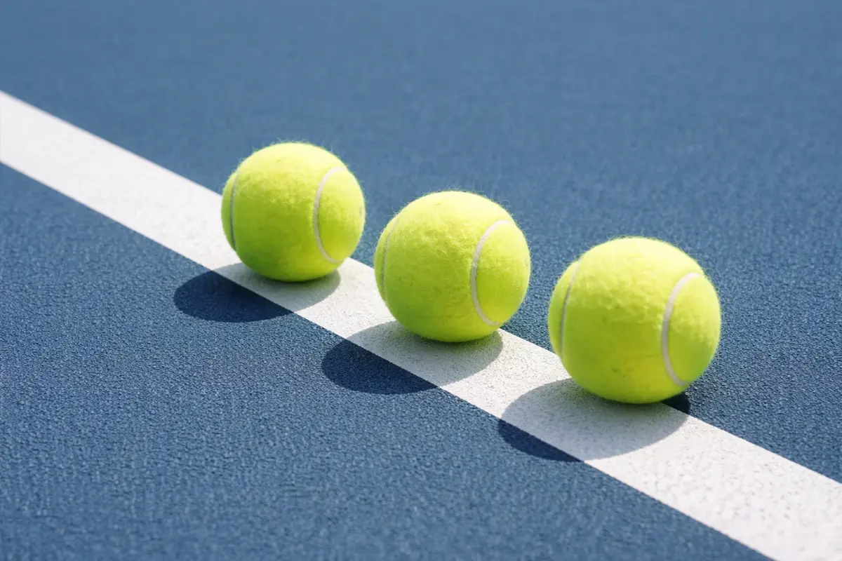 Tre palline da tennis allineate su un campo in cemento accanto alla linea bianca